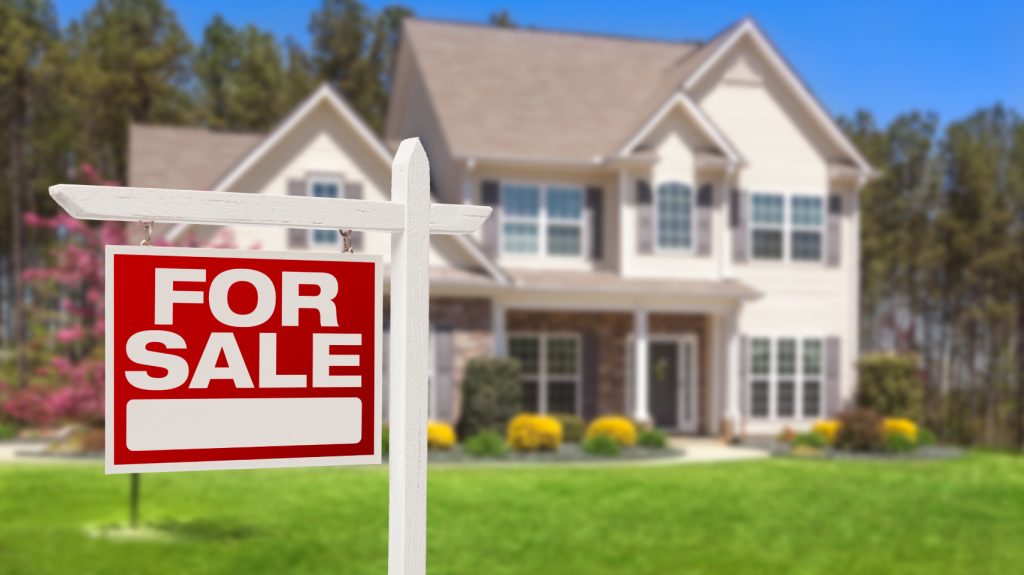 For Sale sign in front of a large house