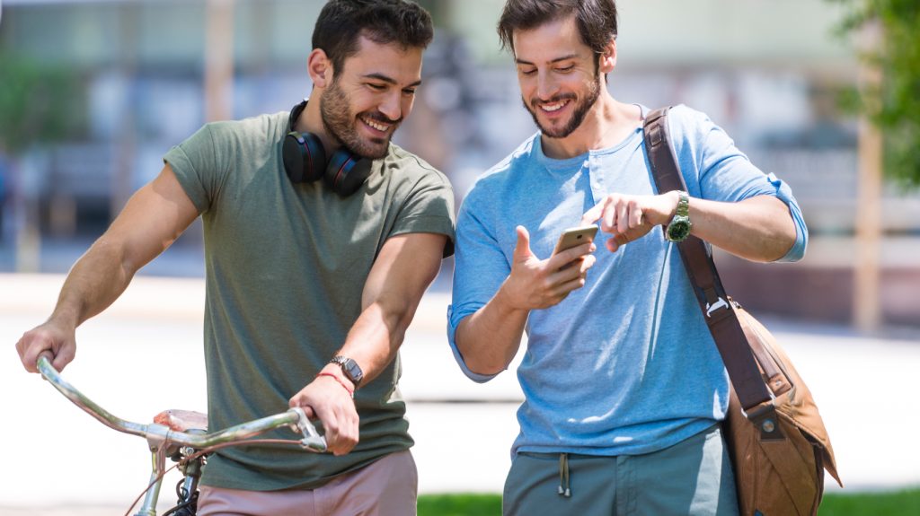 Man showing phone to friend while walking through city.