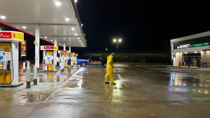 Employee pressure washing a gas station parking lot.